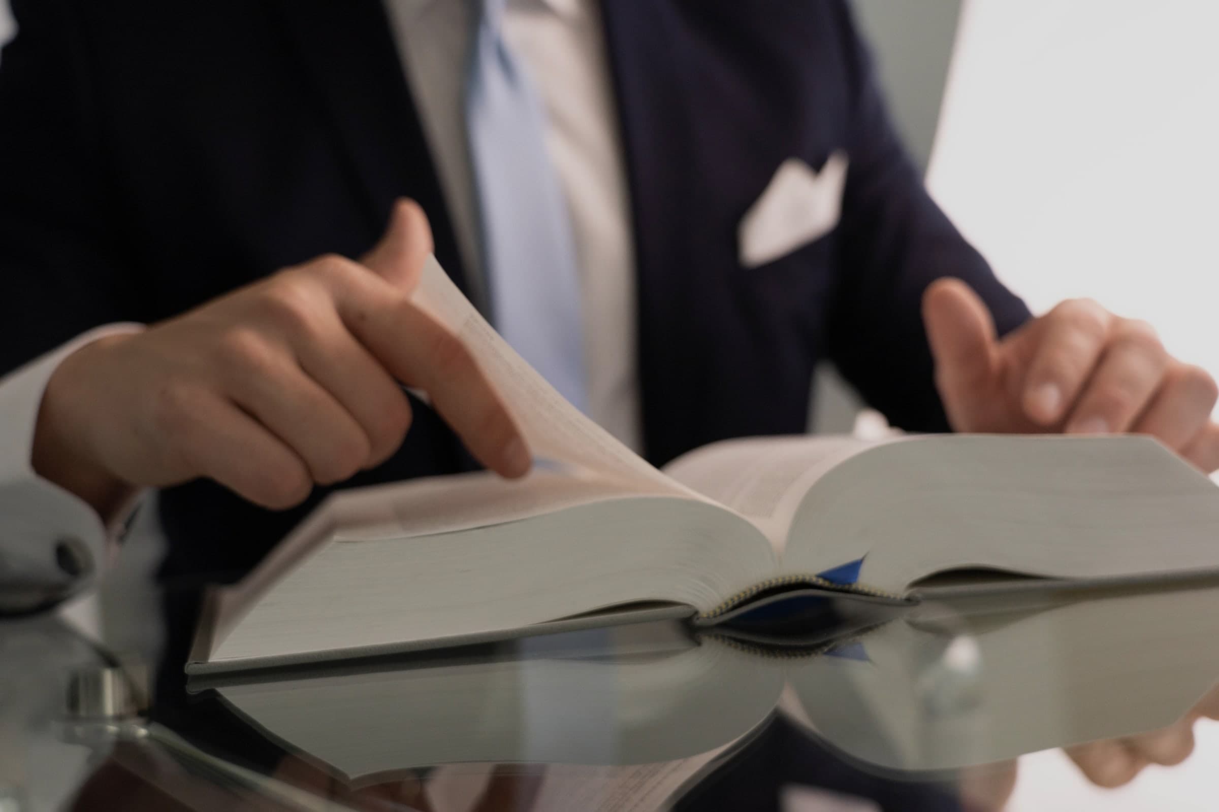 Hands turning the pages of an open book on a glass desk