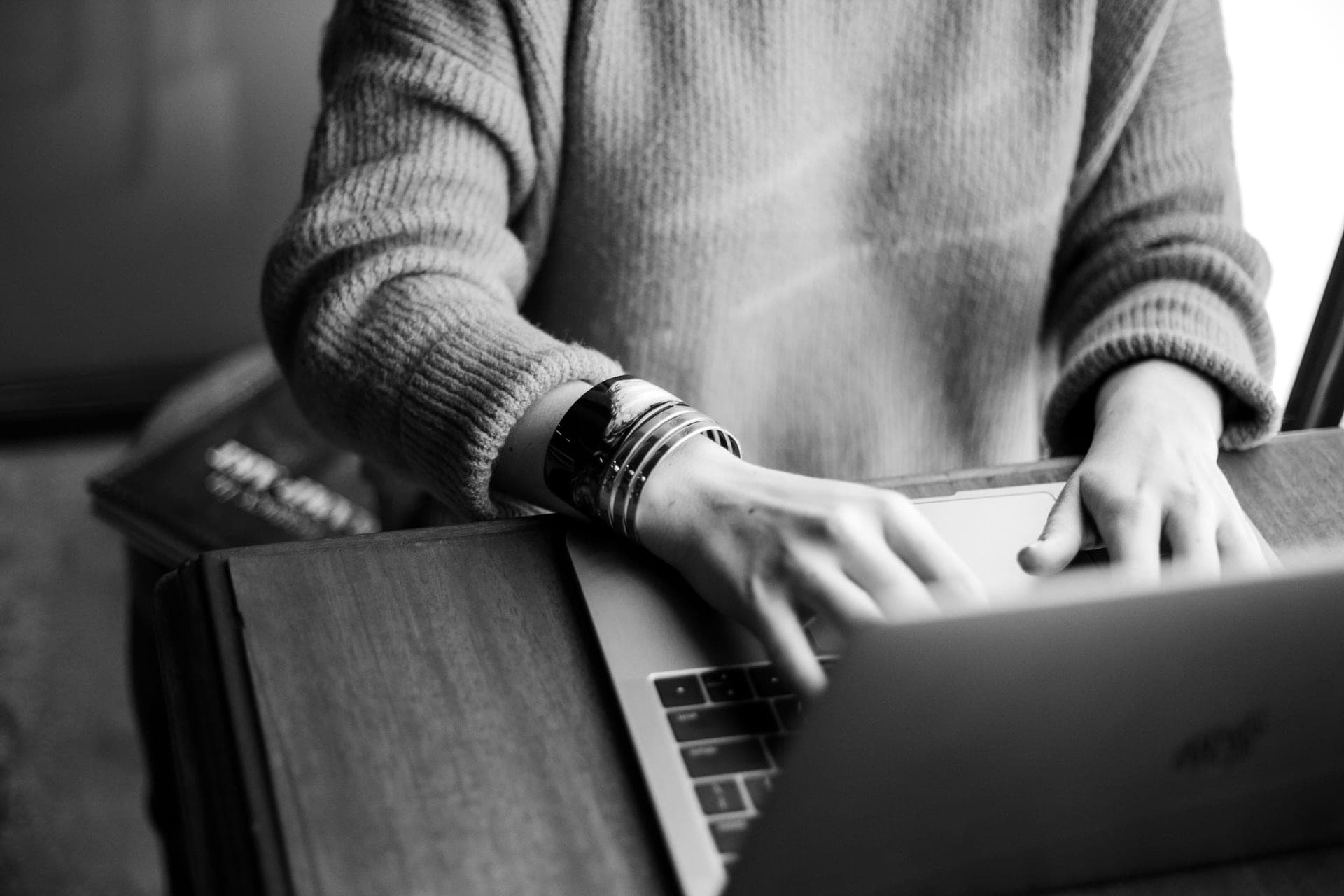 Black-and-white photograph of a person typing on a laptop resting on their knees