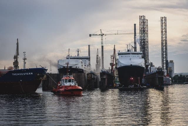 Ships and a red tugboat in a harbour beneath tall cranes