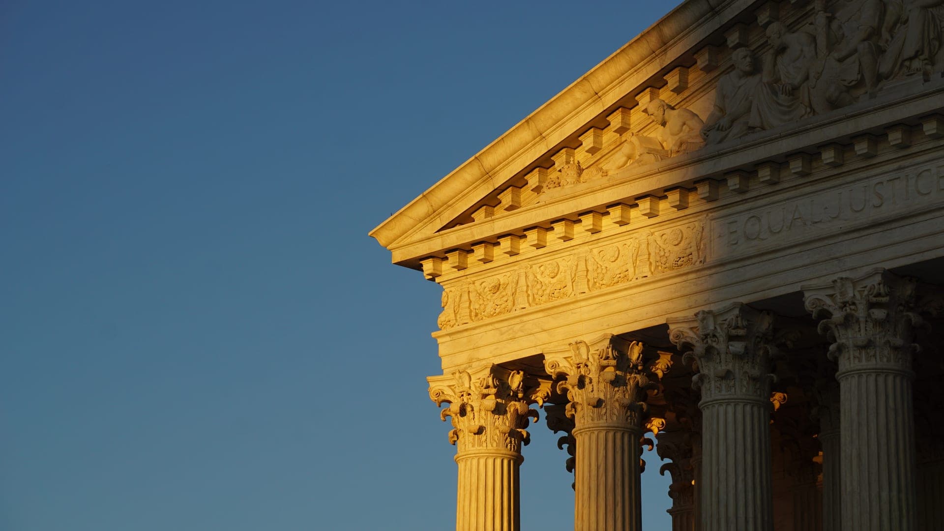 Sunlit columns and pediment of a neoclassical building against a blue sky